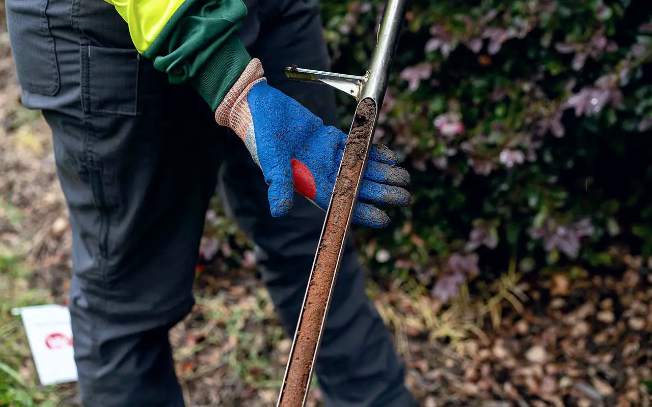 Gloved hand taking a soil sample with a probe